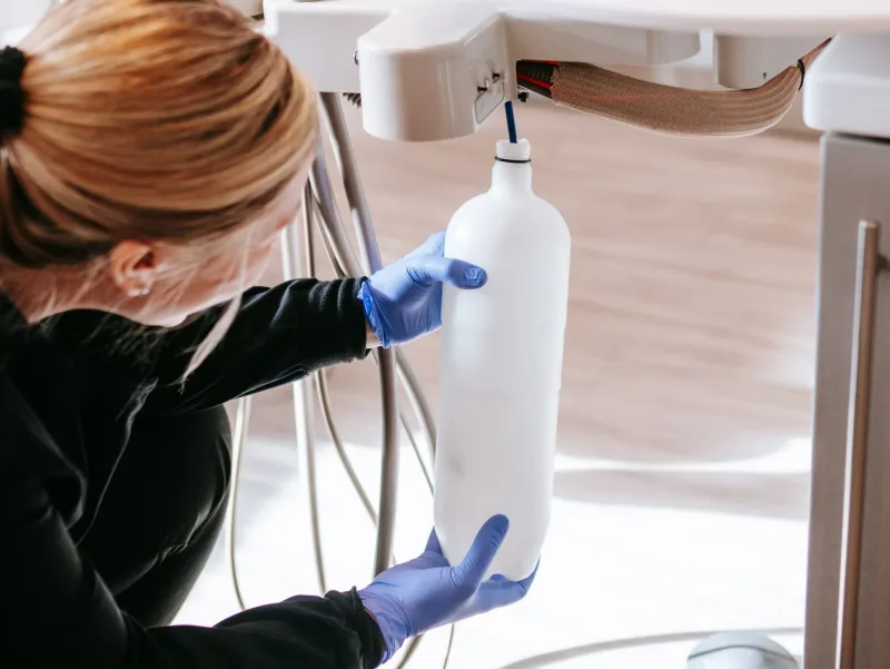 A dental assistant placing a dental water bottle back on the dental unit